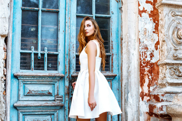Beautiful girl in a white dress near a blue door - Fotoğraf, Görsel