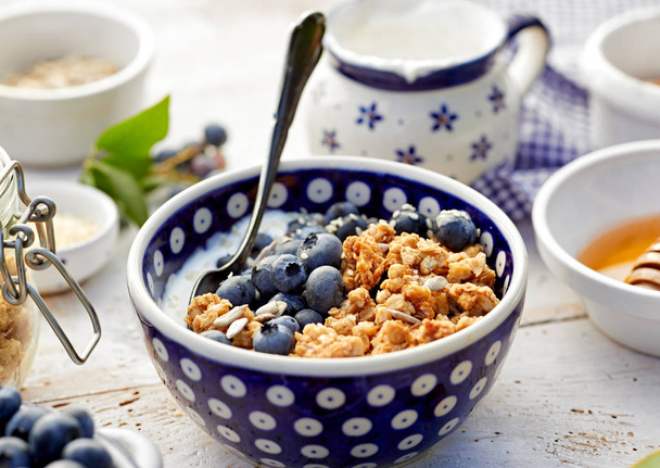 Granola with natural yogurt, fresh blueberries, nuts and honey in a ceramic bowl. Delicious breakfast or dessert.  Healthy eating concept. - Fotó, kép