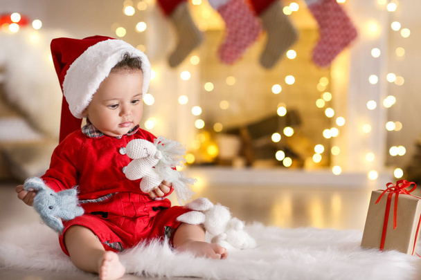 Cute little baby with Santa hat and toys sitting on floor in decorated for Christmas room - Foto, imagen