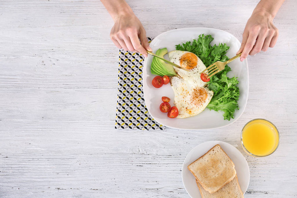 Woman eating tasty breakfast with fried eggs on white wooden table - Foto, Imagem