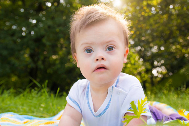 Porträt eines süßen Jungen mit Down-Syndrom, der an einem Sommertag auf einer Decke in der Natur liegt - Foto, Bild