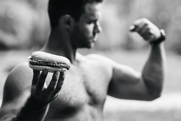 A man holds a burger and shows a biceps - Фото, зображення
