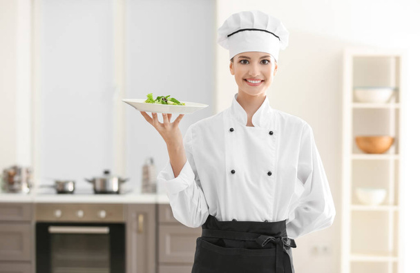 Young female chef holding plate with salad in kitchen - Fotografie, Obrázek