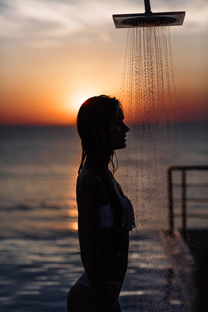 силуэт красивой девушки с идеальной фигурой в душе на закате в море и бассейне
 - Фото, изображение