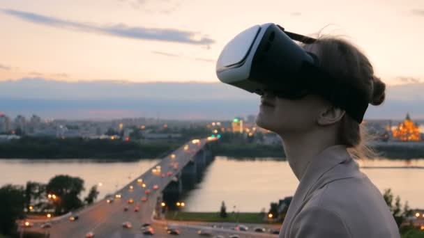Mujer utiliza gafas de realidad virtual en la ciudad después del atardecer
 - Metraje, vídeo