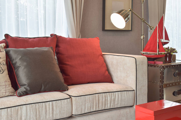 Classico soggiorno dall'aspetto industriale con divano beige e cuscini in lino rosso e marrone scuro con lampada da lettura in ottone
 - Foto, immagini