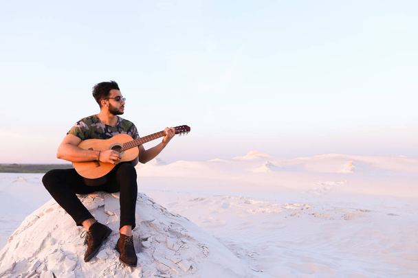Attractive Arabian guy sings songs on guitar, sitting on hill in - Photo, Image
