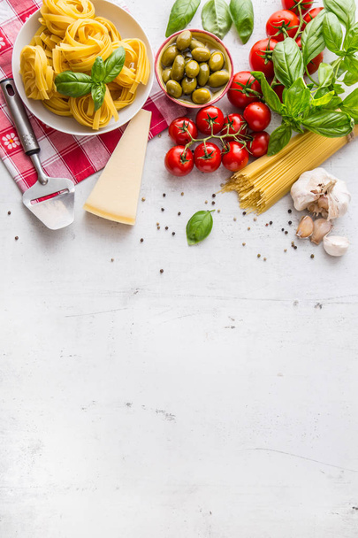 Italian food cuisine and ingredients on white concrete table. Spaghetti Tagliatelle olives olive oil tomatoes parmesan cheese garlic pepper and basil leaves and checkered tablecloth. Free space for your text or information - Foto, Bild