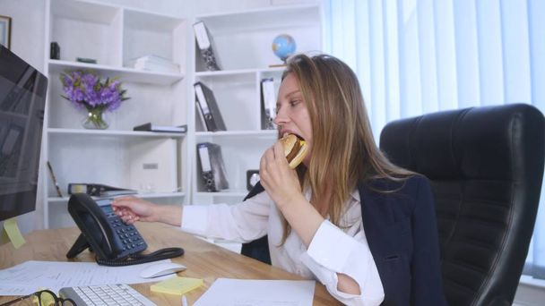 Busy woman talking on the phone while having burger - Fotoğraf, Görsel