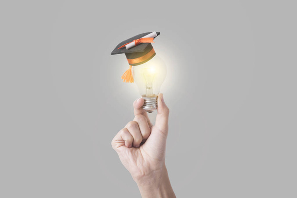 Studentin hält Glühbirne mit Diplomhut auf grau  - Foto, Bild