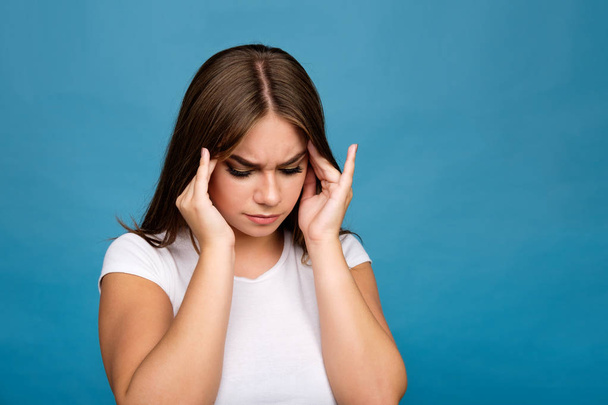 jonge brunette meisje in wit t-shirt lijden aan hoofdpijn,  - Foto, afbeelding