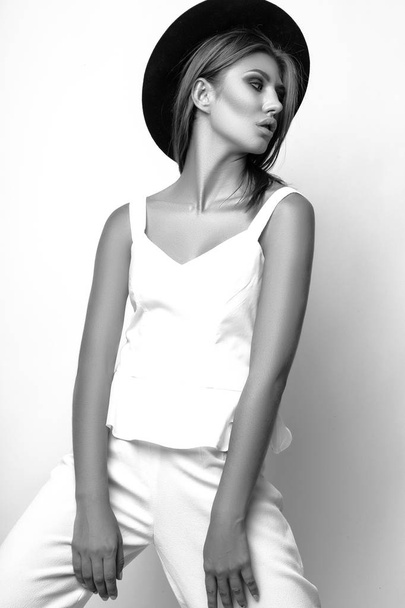 Girl in a white suit and black hat in the studio on a white background. Black and white photo - Φωτογραφία, εικόνα