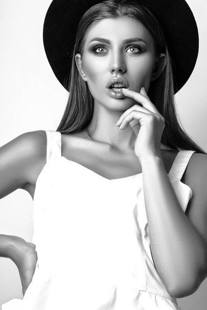 Girl in white clothes and black hat posing in studio on white background. Black and white phot - Foto, Imagem