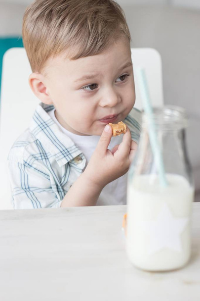 Un petit garçon mignon mange des bonbons et boit du lait. La santé. Joyeux enfant. Petit déjeuner. Un petit garçon est assis à la table
. - Photo, image