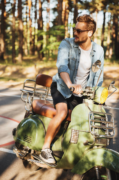 Concentrated young bearded man sitting on scooter outdoors - Фото, зображення