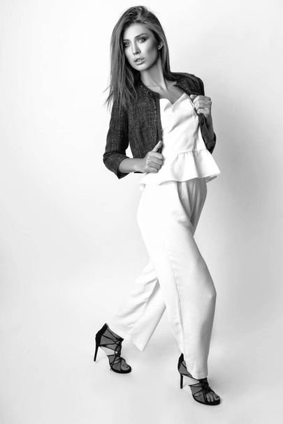 Young woman dressed in white clothes and blue jacket posing in studio on a white background. Black and white phot - Foto, imagen