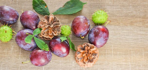 Autumn fruits, cone, chestnuts, plum and leaves on wood backgrou - 写真・画像