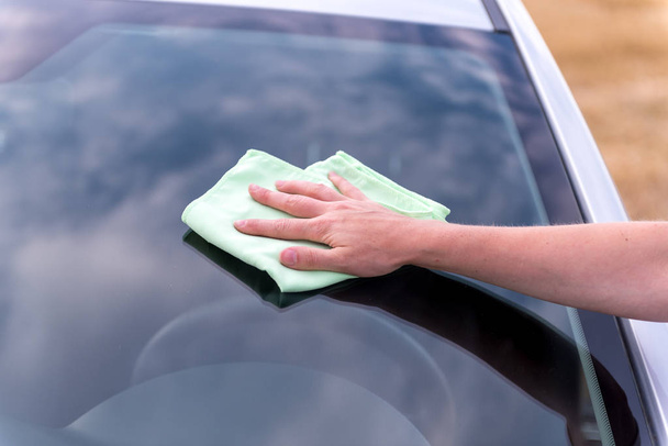 Woman's hand with rag cleaning a silver car's windshield in sunn - Foto, imagen