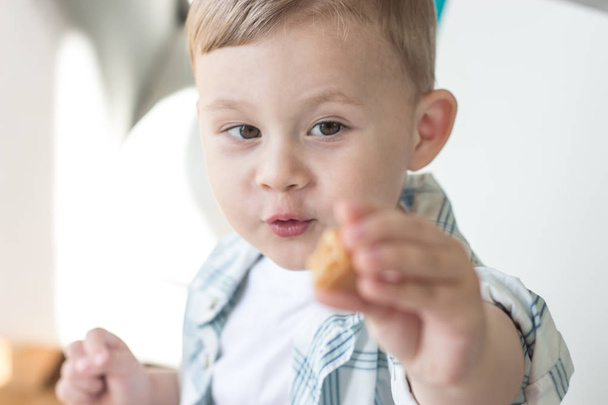 Een schattige kleine jongen is het eten van snoep en drinken van melk. Gezondheid. Gelukkig kind. Ontbijt. Een jongetje zit aan de tafel. - Foto, afbeelding