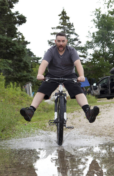 mężczyzna jedzie na rowerze przez kałuża  - Zdjęcie, obraz