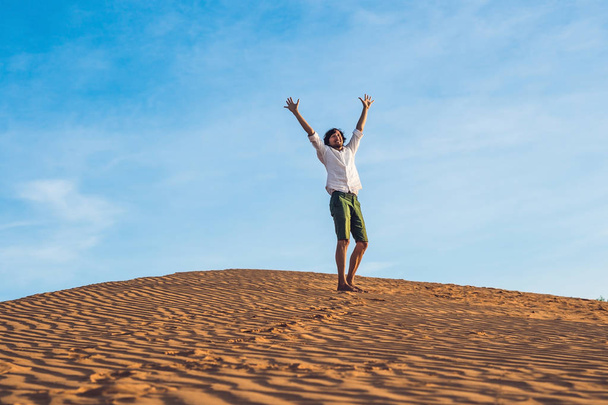 Beautiful young man jumping barefoot on sand in desert - Φωτογραφία, εικόνα