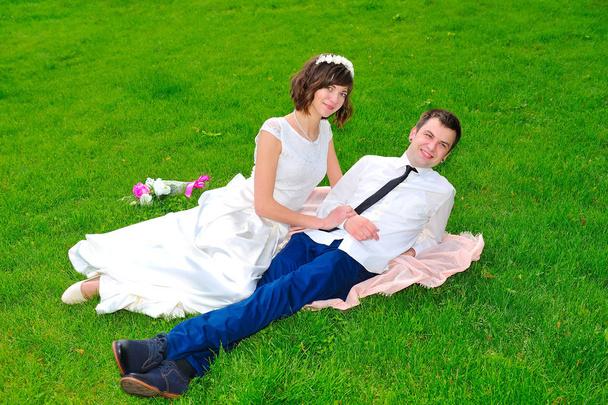 緑の芝生に横たわる若くてハンサムな新婚夫婦 - 写真・画像