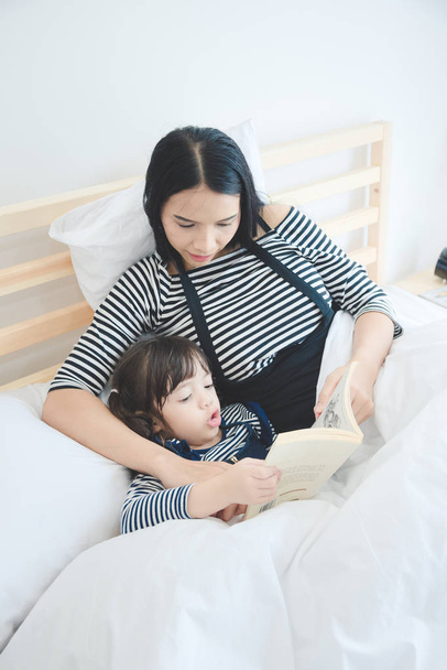 feliz amor familia joven asiático madre enseñando su hija a leer un cama tiempo cuento libro
 - Foto, imagen