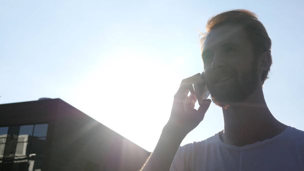 Caminar y hablar por teléfono durante el atardecer, frente al sol
 - Foto, imagen
