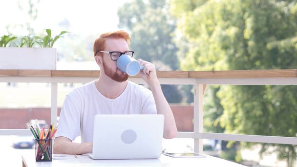 Tomar un sorbo de café caliente, Beber mientras está sentado en la oficina al aire libre, Cabellos Rojos
 - Foto, Imagen