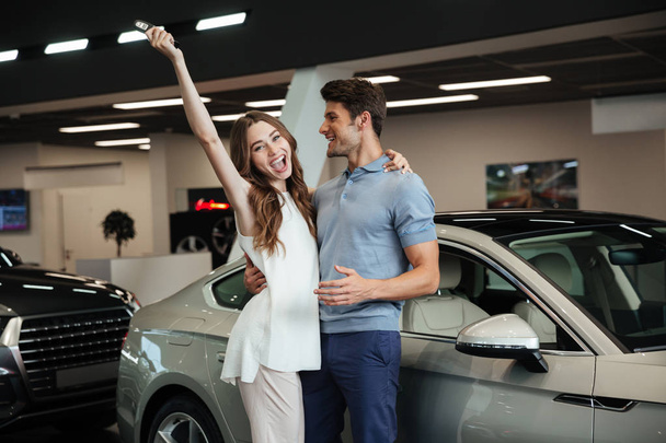 Lovng couple standing near car in car dealership. - Foto, Bild