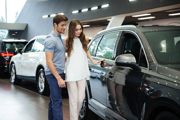 Beautiful young couple standing at the car dealership - Foto, afbeelding