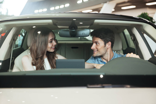 Smiling excited couple sitting inside a new car - Foto, afbeelding