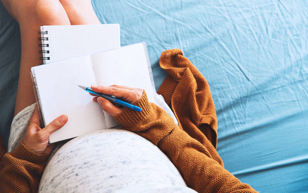 Pregnant woman makes notes and looking at medical documents.  - Фото, изображение