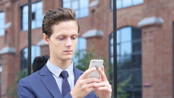 Homme d'affaires utilisant un smartphone pour rechercher des informations, debout à l'extérieur
 - Photo, image