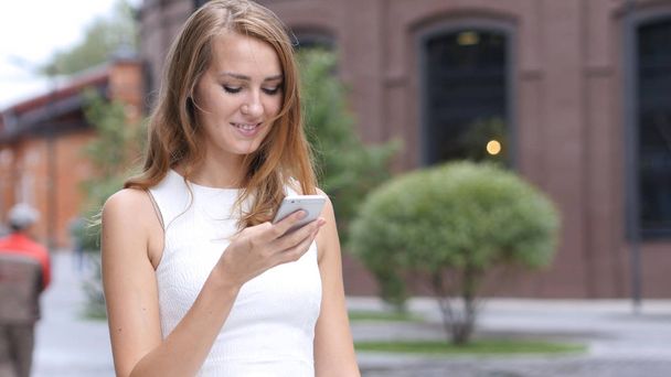 Mensagens de texto no smartphone por menina bonita, fora do escritório
 - Foto, Imagem