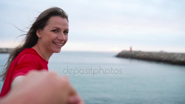 Suivez-moi - heureuse jeune femme en robe rouge tirant les gars main dans la main marchant vers le phare sur la plage au coucher du soleil
. - Séquence, vidéo