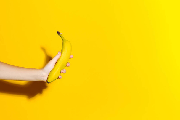 La mano femenina sobre un fondo amarillo sostiene un plátano fresco
 - Foto, Imagen
