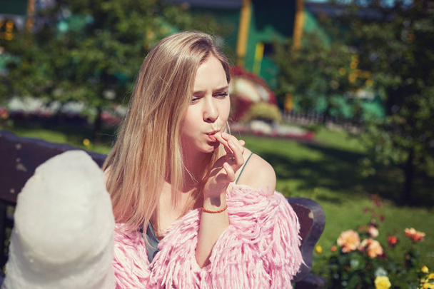Instagram filter. Close up portrait of tender blond student eating white huge candy cotton with passion. Young & carefree beautiful female hipster traveler is taking rest outdoors in summer city park. - Photo, Image