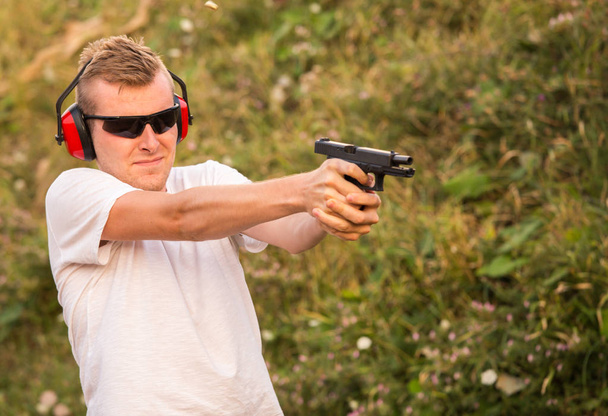 Young blonde handsome guy shooting from fire arms gun violent gl - Photo, Image