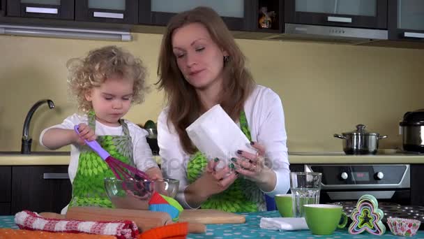 Ładna dziewczyna z matką mieszania mąki czekolady w szklanej misce na stole w kuchni - Materiał filmowy, wideo