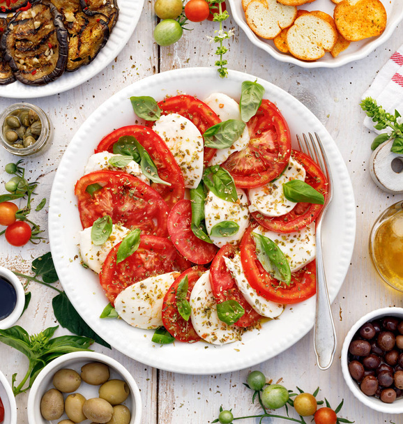 Salade de caprese à base de tomates fraîches tranchées, fromage mozzarella et basilic servi sur une assiette blanche sur une table en bois.
 - Photo, image
