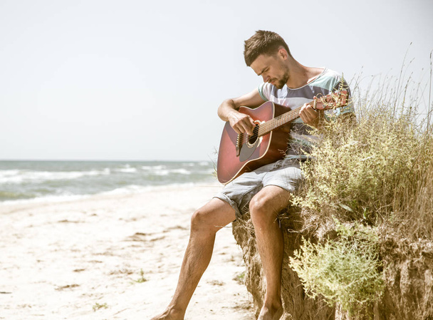 молодой человек с акустической гитарой на пляже, концепция досуга и творчества
 - Фото, изображение