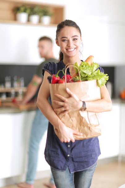 Young couple in the kitchen , woman with a bag of groceries shopping - Фото, изображение