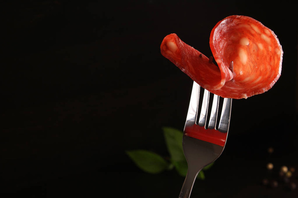 Salami Spain sausage Salchichon on a fork on a dark black backgr - Photo, image