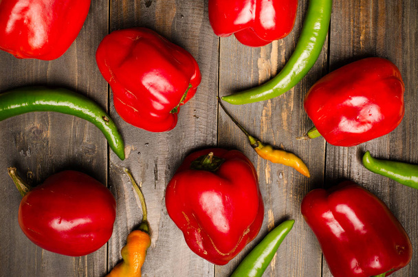 Red bell peppers and green chili on wooden background - 写真・画像