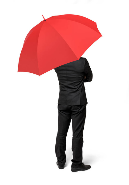 Ізольований бізнесмен, що стоїть зі спиною, повернутою під червону парасольку
. - Фото, зображення