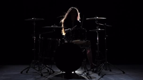 Girl is kicks from playing drums, playing energetic music. Black background. Silhouette. Slow motion - 映像、動画