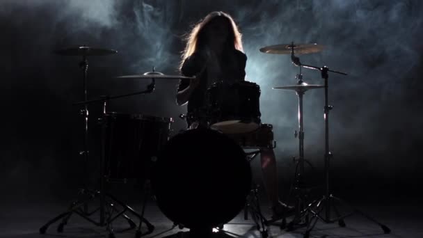Girl is kicks from playing drums, playing energetic music. Black smoke background. Silhouette. Slow motion - Кадри, відео