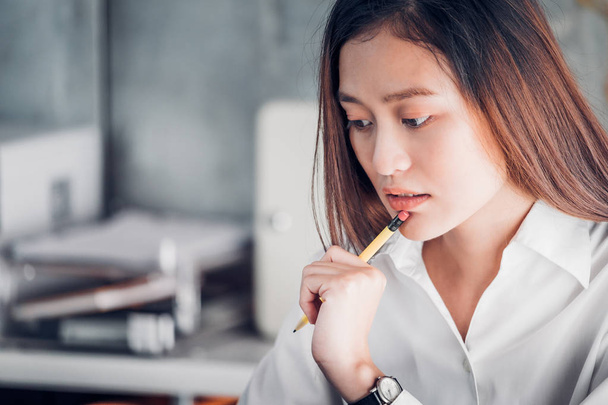 Asian businesswoman thinking with pencil and looking down to lap - Фото, зображення