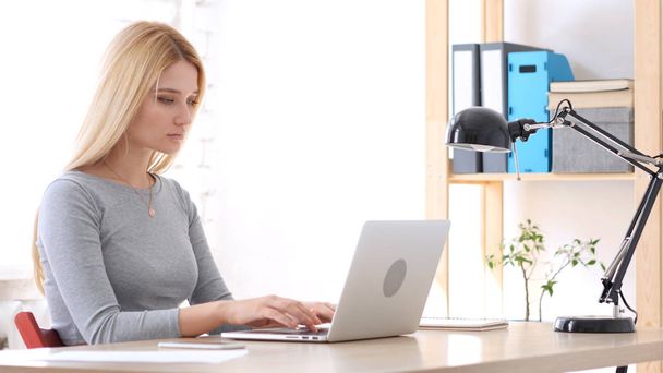 Jonge vrouw werkt op laptop in kantoor - Foto, afbeelding
